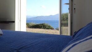 Een slaapkamer met een bed, een deur naar een balkon met uitzicht op zee en bergen.