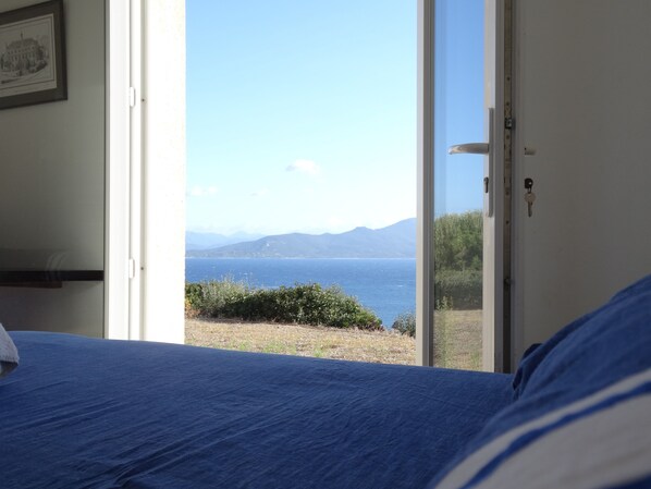 A bedroom with a bed, a door leading to a balcony with a view of the sea and mountains.