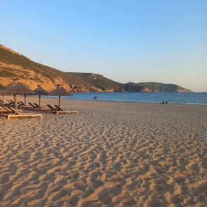 A beach with sun loungers and umbrellas, a clear sky, and a calm sea.