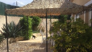 Ein überdachter Außenbereich mit Steinboden, einer Pergola mit gemustertem Dach und verschiedenen Kübelpflanzen.