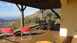 Un terrazzo in legno con tavolo e sedie, affacciato su un paesaggio montuoso.