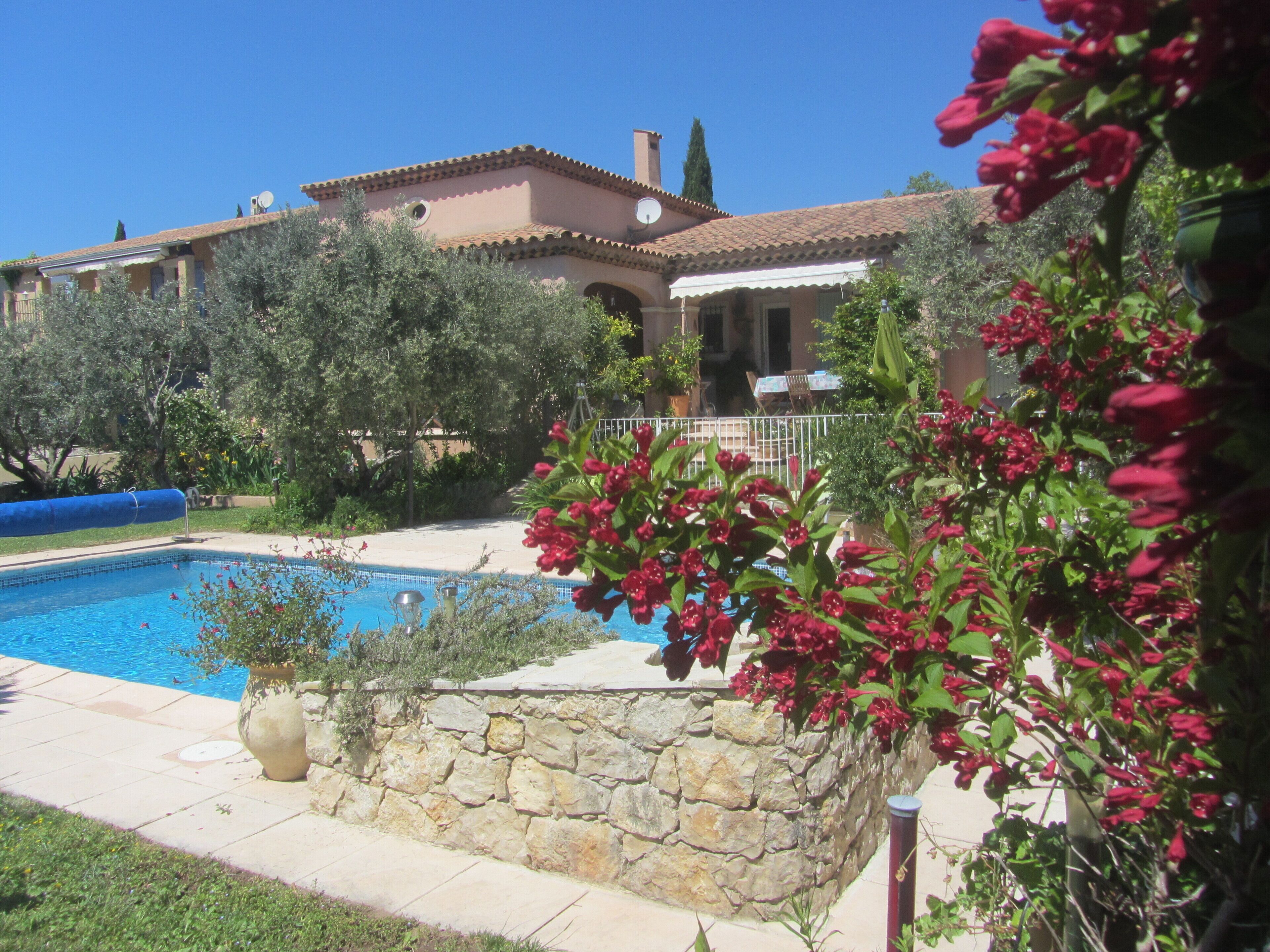 A pool surrounded by stone walls and lush greenery, with a building in the background.