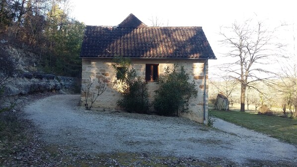 A small stone house with a tiled roof, a window, and a gravel path leading to it.