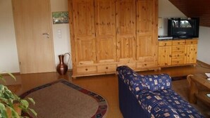 Ein gemütliches Zimmer mit einem Holzschrank, einem Fernseher auf einer Holzkommode, einem gemusterten Sofa und einem kleinen Teppich.