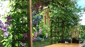 Un tavolo di legno con una panca, circondato da vegetazione lussureggiante e fiori viola.