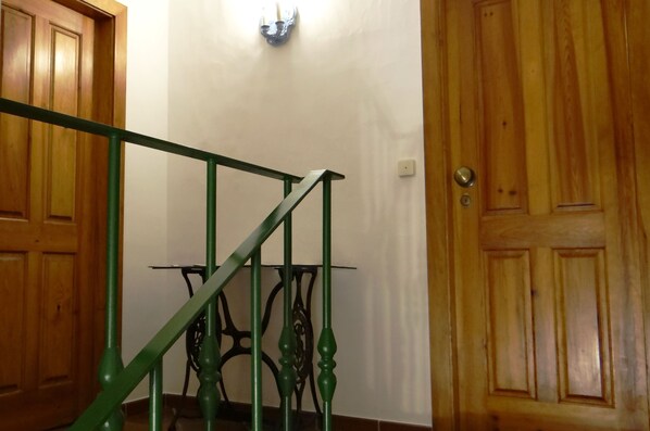 A wooden door with a brass doorknob, a green metal staircase railing, and a wall-mounted light fixture. - CASA SÃO JOÃO T0 - Cozy studio 100 m from the beach (PENICHE)