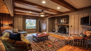 A cozy living room with a fireplace, wooden beams, a television, and comfortable seating.
