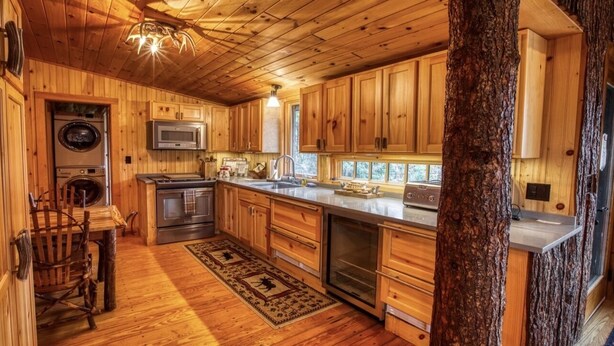 A wooden cabin interior with a kitchen featuring wooden cabinets, a microwave, a washing machine, and a dishwasher.
