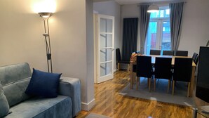 Ein Wohnzimmer mit grauem Sofa, einer Stehlampe und einem Essbereich mit Tisch und Stühlen.
