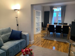 Una sala de estar con un sofá gris, una lámpara de pie y un comedor con una mesa y sillas.