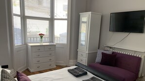 Ein Schlafzimmer mit Bett, Kommode, Fernseher und einem Fenster mit Jalousien.