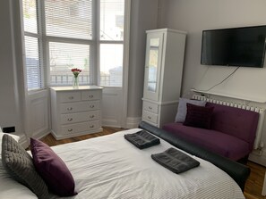 Un dormitorio con cama, cómoda, televisor y ventana con persianas.