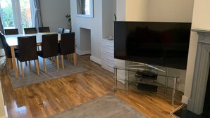 Ein modernes Wohnzimmer mit Flachbildfernseher, Holzboden, einer Essecke mit Tisch und Stühlen und einem Kamin.