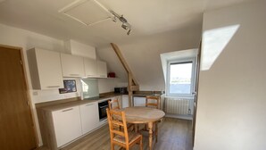 A compact kitchen with white cabinets, a wooden dining table, and a view through a window. - Apartment 1ST Floor, SEA View (Paimpol)