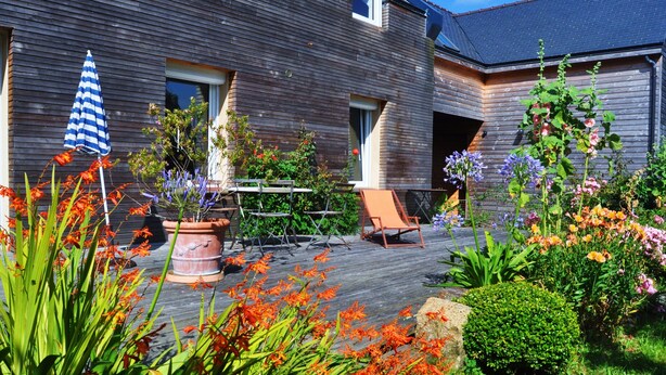 A wooden deck with a chair and a table, surrounded by various potted plants and flowers. - Apartment 1ST Floor, SEA View (Paimpol)