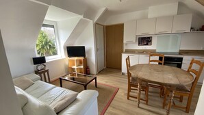 A compact living space with a sofa, a dining table with chairs, a TV, and a kitchenette. - Apartment 1ST Floor, SEA View (Paimpol)