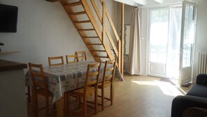 A dining area with a wooden table and chairs, a staircase, and a large window with curtains. - Quiet house between countryside and sea surrounded by green setting (Rouillé)