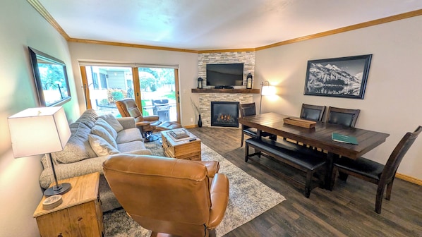 A living room with a fireplace, a television mounted above it, and a dining table with chairs.