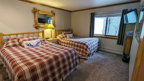 Une chambre avec deux lits, une tête de lit en bois, un miroir, une lampe et une fenêtre avec des rideaux.