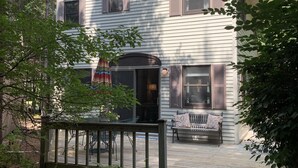 Een woonhuis met twee verdiepingen, een overdekte veranda, een voordeur en een bankje.