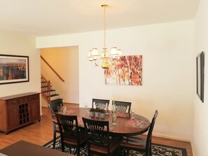 A dining area with a round table, chairs, and a chandelier. There is a staircase in the background and a framed picture on the wall. - Newly furnished, large, bright, beach house in the heart of it all! (Lewes)