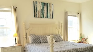 Un dormitorio con cama, mesita de noche, lámpara, ventilador de techo y una obra de arte en la pared.