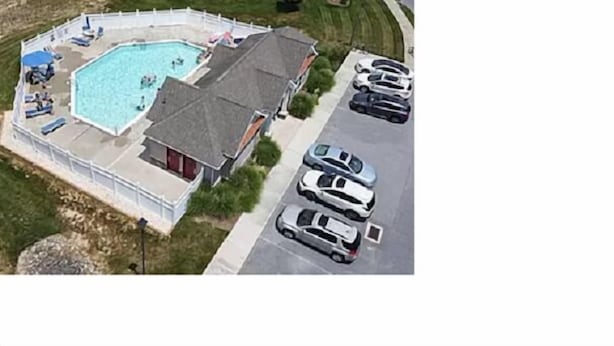 Vista aérea de una propiedad residencial con piscina, un patio cubierto y un estacionamiento con varios coches.