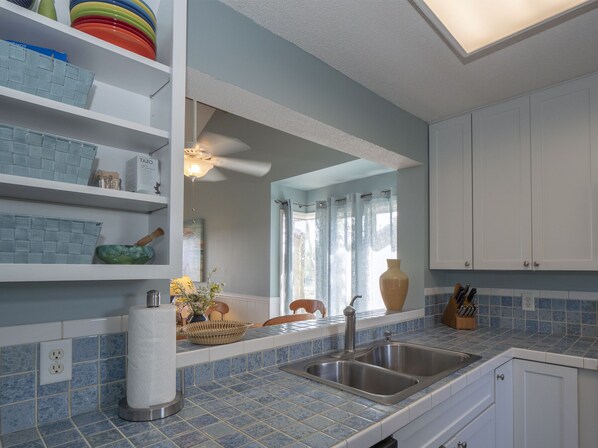 A kitchen with blue tiles, white cabinets, a double sink, and a ceiling fan.