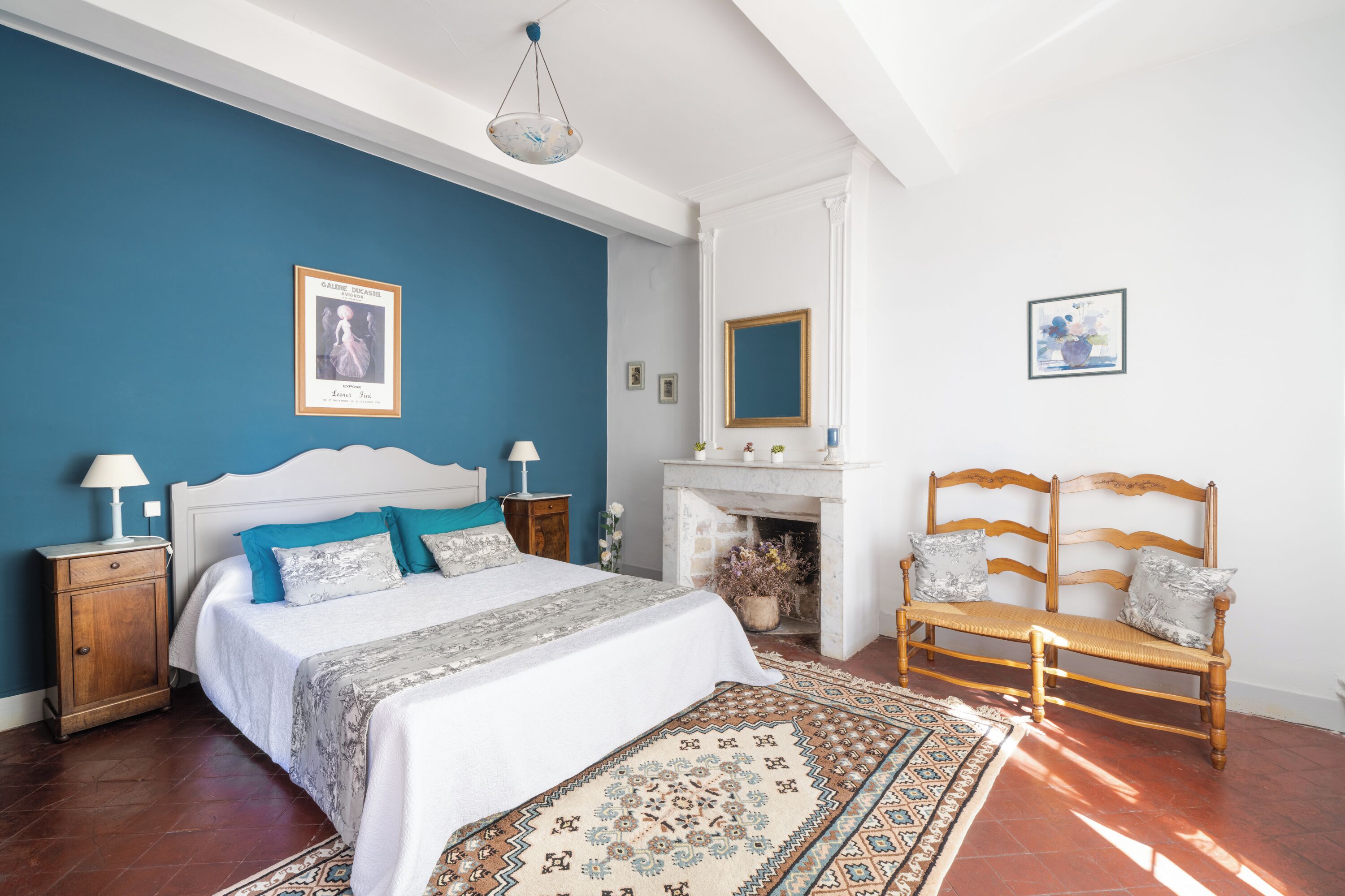 A bedroom with a bed, a wooden bench, a fireplace, and a blue accent wall.