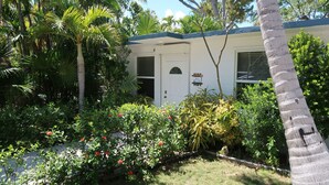 A house with a white exterior, a blue roof, and a small garden with various plants and flowers. - Keys Kottage & Bayside Villa W/ free onsite boat ramp marina & trailer parking. (Islamorada)