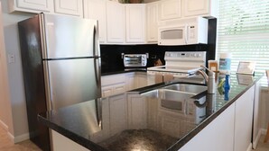 A modern kitchen with stainless steel appliances, a black countertop, and white cabinetry. - Keys Kottage & Bayside Villa W/ free onsite boat ramp marina & trailer parking. (Islamorada)