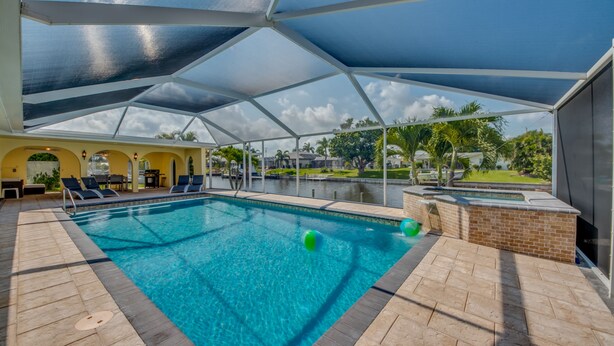 A swimming pool with a covered area, lounge chairs, and a view of a landscaped garden.
