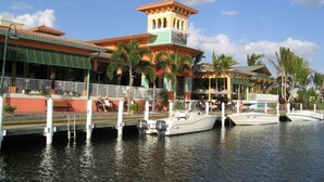 A waterfront hotel with a tower, docked boats, and outdoor seating areas.