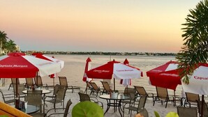 A beachside restaurant with outdoor seating and umbrellas, overlooking the sea.
