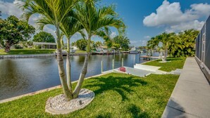 A waterfront property with a grassy lawn, palm trees, a dock, and boats.