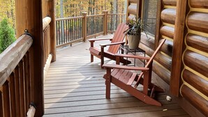 Una terraza de madera con dos mecedoras y una mesa, con vista a un bosque otoñal.