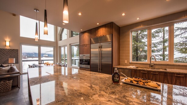 A modern kitchen with a large island, stainless steel appliances, and large windows offering views of the outdoors. - TRUE ski in/out. ski_bike_hike to BOTH Gondolas-Pvt HotTub VIEWS-walk everywhere (Whistler)