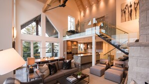 A spacious living area with a high ceiling, a staircase, and a kitchen in the background. - TRUE ski in/out. ski_bike_hike to BOTH Gondolas-Pvt HotTub VIEWS-walk everywhere (Whistler)