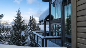 A modern building with large windows and a balcony, surrounded by snow-covered trees and mountains. - TRUE ski in/out. ski_bike_hike to BOTH Gondolas-Pvt HotTub VIEWS-walk everywhere (Whistler)
