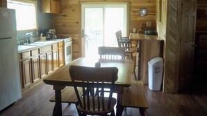 A wooden cabin kitchen with a dining table, chairs, a refrigerator, and a stove.