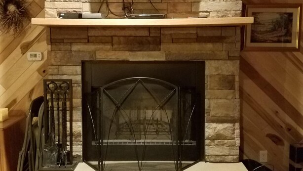 A stone fireplace with a flat-screen TV mounted above it, surrounded by wooden beams.