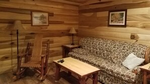 A cozy cabin interior with wooden walls, a floral sofa, a wooden table, and a rocking chair.