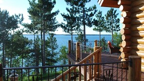 A wooden deck with a railing overlooking a lake, surrounded by trees. - Private, Exclusive Lodge on Woman Lake with Beautiful Views (Longville)