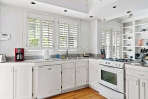 Una cucina con mobili bianchi, forno integrato, piano cottura e macchina per il caffè.