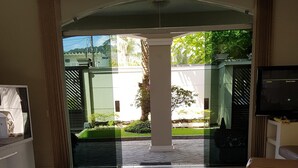 A modern living room with a sofa, a coffee table with magazines, a TV, and a view of a garden through a glass door. - Guarujá, Pernambuco Beach, a 3-minute walk from the beach. A paradise on the beach! (Balneario Praia do Pernambuco)