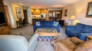 A living room with a blue sofa, a wooden coffee table, and a TV. - Remodeled Condo w/ FREE WiFi, Parking, Heated Pool, Hot Tubs, Skier Shuttles (Avon)