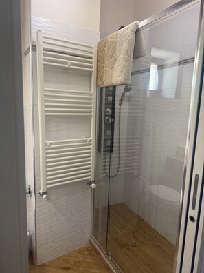 A glass-enclosed shower with a white towel rack, a glass shower door, and a wooden floor.