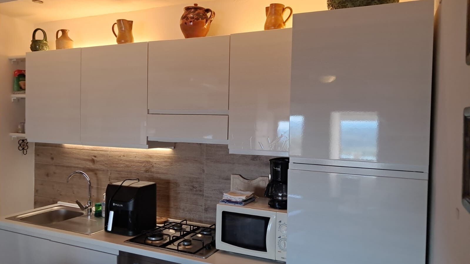 Una cocina con armarios blancos, estufa a gas, microondas y cafetera.