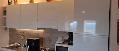 Una cocina con armarios blancos, estufa a gas, microondas y cafetera.
