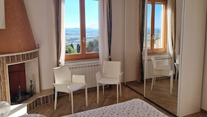 A bedroom with a fireplace, two chairs, a bed, a large mirror, and a view of the countryside. - La Terrazza sulla Valle, with private terrace overlooking the valley! (Cortona)